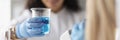 Woman chemist holding glass beaker with blue liquid in front of microscope in laboratory Royalty Free Stock Photo