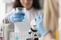 Woman chemist holding glass beaker with blue liquid in front of microscope in laboratory Royalty Free Stock Photo