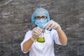 Woman chemist in protective uniform making experiment with blue and yellow flask