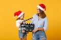 Woman child girl in Christmas Santa hat hold clapperboard. Mommy little kid daughter isolated on yellow background Royalty Free Stock Photo