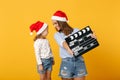 Woman child girl in Christmas Santa hat hold clapperboard. Mommy little kid daughter isolated on yellow background Royalty Free Stock Photo