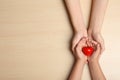 Woman and child holding heart on beige wooden background, top view. Donation concept