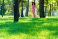 Woman and child walk in a city park, summer day, green lawn with grass and trees, bright sunlight and shadows Royalty Free Stock Photo