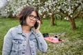 A woman with children looks at a grazing cow on the background of a blooming garden and green grass. Blanket with laptop and