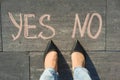 Woman before the choice yes or no. View from above, female feet with text yes no written on grey sidewalk. Royalty Free Stock Photo