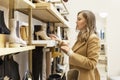 Woman chooses elegant shoes in the store. Young beautiful blonde in a beige coat. Style and fashion. Side view Royalty Free Stock Photo