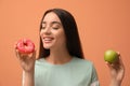 Woman choosing between apple and doughnut on orange background Royalty Free Stock Photo