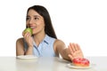 Woman choosing between apple and doughnut at table on white background Royalty Free Stock Photo