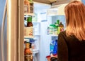 Woman choosing food from open refrigerator