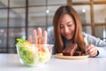 A woman choosing to eat brownie cake and making hand sign to refuse a vegetables salad Royalty Free Stock Photo