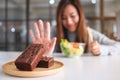 A woman choosing to eat vegetables salad and making hand sign to refuse a brownie cake Royalty Free Stock Photo