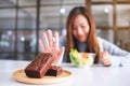 A woman choosing to eat vegetables salad and making hand sign to refuse a brownie cake Royalty Free Stock Photo