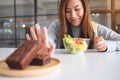 A woman choosing to eat vegetables salad and making hand sign to refuse a brownie cake Royalty Free Stock Photo