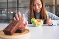 A woman choosing to eat vegetables salad and making hand sign to refuse a brownie cake Royalty Free Stock Photo