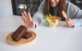 A woman choosing to eat vegetables salad and making hand sign to refuse a brownie cake Royalty Free Stock Photo
