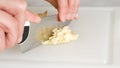 A woman chops fresh garlic using a kitchen knife on a white plastic cutting board Royalty Free Stock Photo