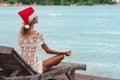 Woman in christmas hat meditating in a yoga pose at thel beach Royalty Free Stock Photo