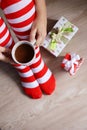 Woman in Christmas knee socks sitting with cup of hot cocoa in hands near the gift boxes, vertical shot