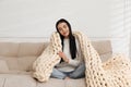 Young woman with chunky knit blanket on sofa at home Royalty Free Stock Photo