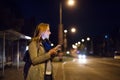 Woman in the city at night holding smartphone, texting. Royalty Free Stock Photo