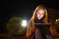 Woman in the city at night holding tablet, reading something. Royalty Free Stock Photo