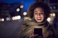 Woman On City Street At Night Ordering Taxi Using Mobile Phone App