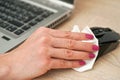 Woman cleaning black computer mouse, about to spray disinfect on it, holding back with paper tissue, closeup detail on hands with