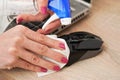 Woman cleaning black computer mouse, about to spray disinfect on it, holding back with paper tissue, closeup detail on