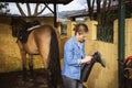 Woman cleaning her riding boots with her brown horse in the background Royalty Free Stock Photo