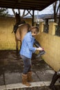 Woman cleaning her riding boots with her brown horse in the background Royalty Free Stock Photo