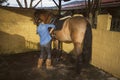 Woman cleaning her riding boots with her brown horse in the background Royalty Free Stock Photo