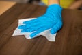 Woman cleaning home office wood table sanitizing surface with wet wipes in blue gloves stock photo