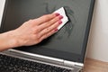 Woman cleaning laptop screen with white tissue, detail on her fingers holding paper towel