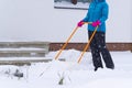 Woman cleaning snow with shovel in winter day. Woman shovelling snow walkway in front of house