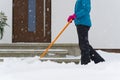 Woman cleaning snow with shovel in winter day. Woman shovelling snow walkway in front of house