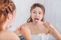 Woman cleaning tongue using toothbrush with mirror in bathroom