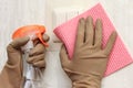 A woman is cleaning a wall, washes a switch. The girl in gloves is holding a cleaning spray and a rag. Cleaning concept