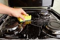 Woman cleans gas stove with a washcloth and foam, surface cleaning, cleaning the kitchen, kitchen appliances Royalty Free Stock Photo