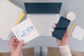 Woman clerk is sitting at office table holding note sticker with message `call mom`