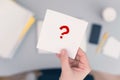 Woman clerk sitting at the office table and holding note sticker with question mark.