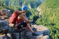 Woman climber with helmet and backpack sits down and relaxes at the end of a via ferrata in Suncuius, Romania, gazing.