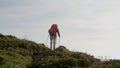 Woman climbing vegetated mountain with trekking poles