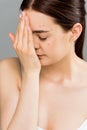 Woman with closed eyes and acne covering face with hand on grey