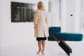 Woman in Coat with Bags in Airport in Waiting Room