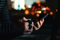 Woman with coffee cup looking at smartphone screen at night