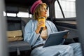 Woman with coffee and digital tablet on backseat of a car Royalty Free Stock Photo