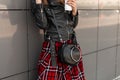 Woman with coffee in fashionable leather jacket and stylish plaid dress with fashion handbag near the wall in the street. Women`s