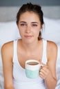 Woman, coffee and portrait in bed for tired in morning for wakeup and drink in cup for warm and strong with milk. Young Royalty Free Stock Photo