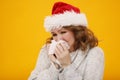 Woman with a cold blowing her runny nose with tissue. Portrait of beautiful girl in winter sweater and Santa Claus hat get sick Royalty Free Stock Photo