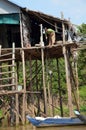 A woman collects water from a river standing in his house on stilts using buckets on a long rope